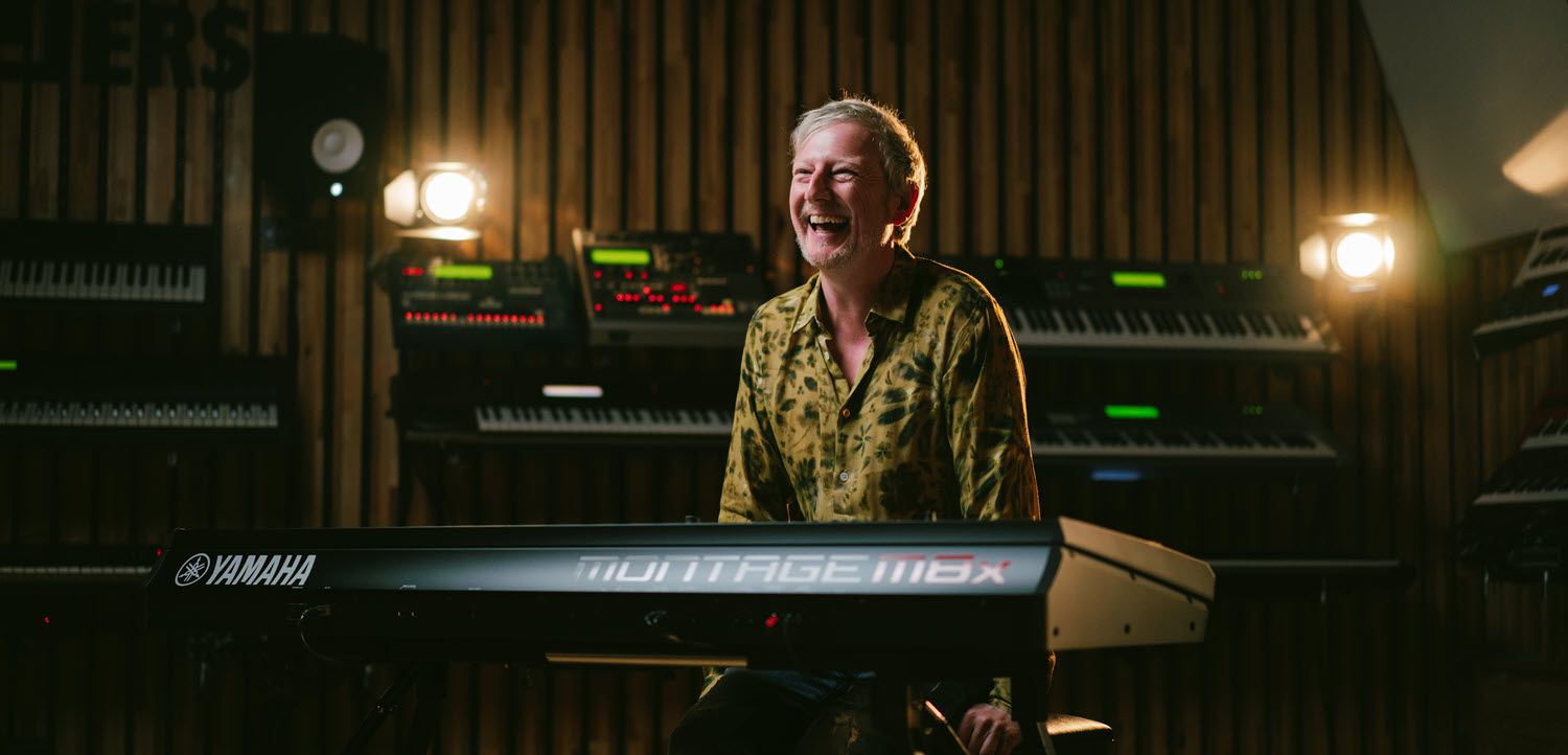 Man smiling while seated at synthesizer.