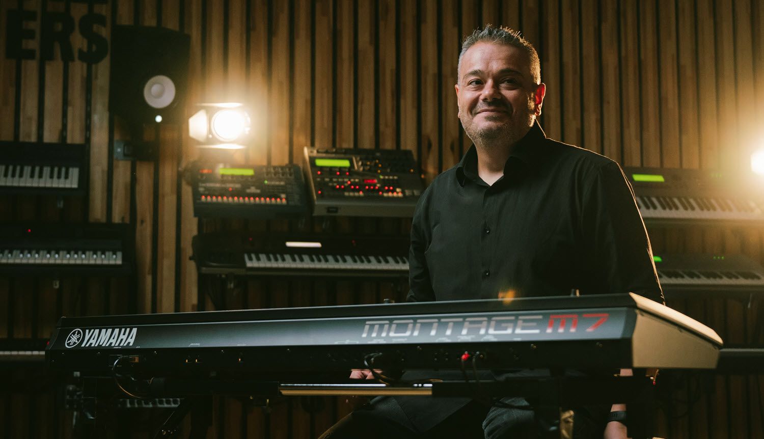 Man seated at synthesizer smiling.